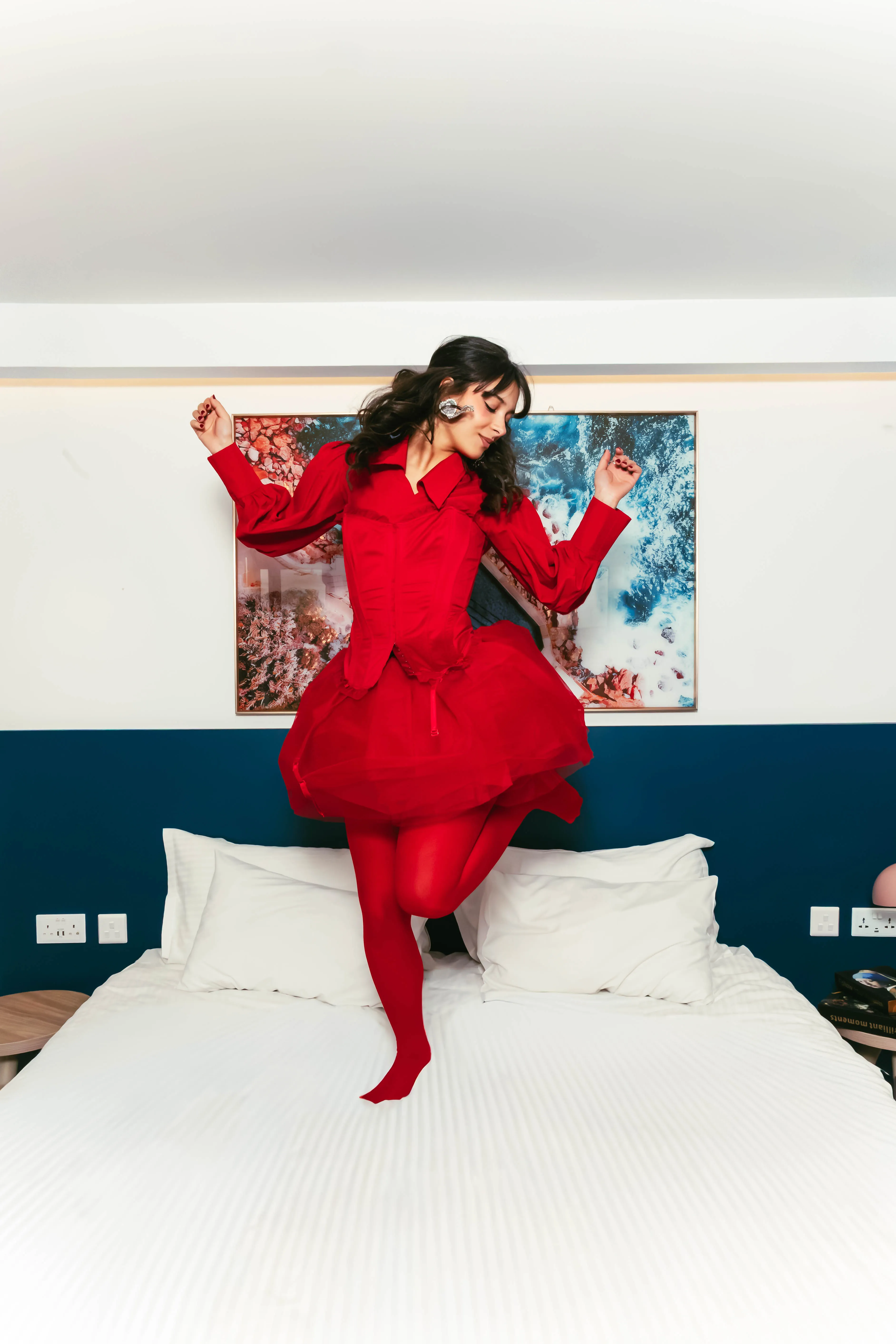 Model in red dress dancing on a hotel bed with ocean art behind