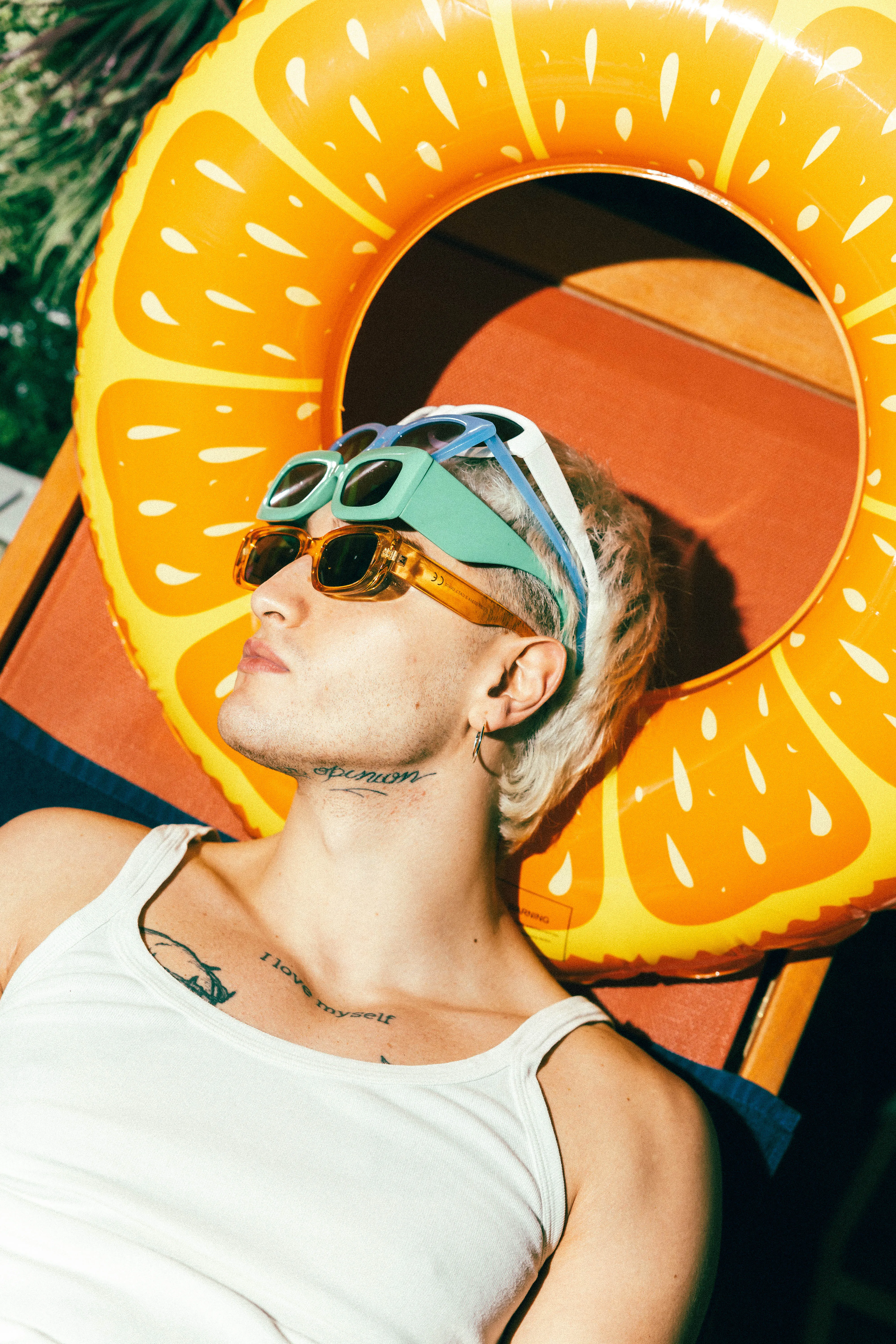 Model with sunglasses relaxing with orange float poolside
